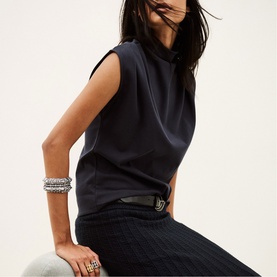 Model wearing Bash blue sleeveless draped neck top, styled with dark wide-leg trousers, silver bangles and a logo belt.