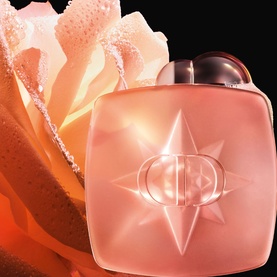 Dior star-embossed peach-toned fragrance bottle with faceted cap, set against a soft pink rose bloom background.