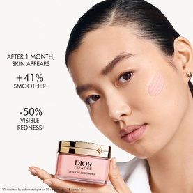 Model with Dior Prestige La Cr&egrave;me de Gommage face scrub applied to cheek, pink jar with gold lid visible, skin stats overlay shown