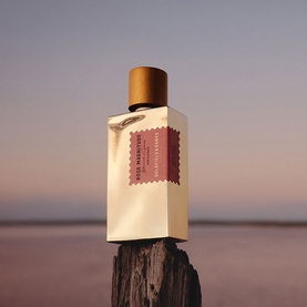Goldfield & Banks Rose Magnitude Eau de Parfum, cream rectangular bottle with gold cap and pink label, on driftwood at dusk