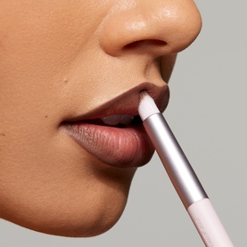 Model with Kylie Cosmetics brush applied to lips, shown in close-up application shot with nude lip look