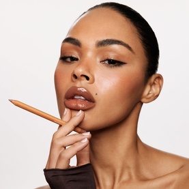 Model with Kylie Cosmetics lip liner pencil held to lips, showcasing a warm nude lip look against a light background.