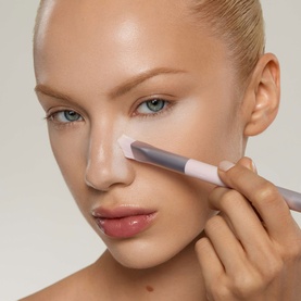 Model with Kylie Cosmetics brush applying product to under-eye area, silver and white brush detail visible