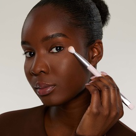 Model with Kylie Cosmetics brush, applying product to cheek. Pink handle with soft bristles, held at cheekbone.