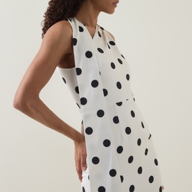 Model wearing Lavish Alice black and white polka dot sleeveless dress with V-neckline, shown from side angle.
