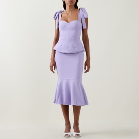 Model wearing Lavish Alice lilac dress with sweetheart neckline, bow shoulder straps, peplum bodice and fishtail hem, styled with white heels