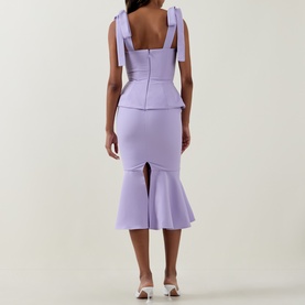 Model wearing Lavish Alice lilac dress, rear view, bow shoulder straps, structured peplum bodice and fluted midi skirt with back split