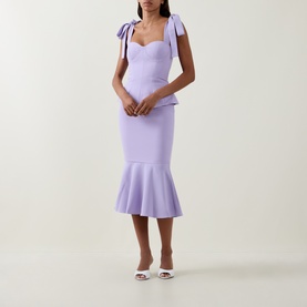Model wearing Lavish Alice Lilac Dress with bow shoulder straps, sweetheart neckline, peplum waist and fishtail hem, styled with white heeled mules.