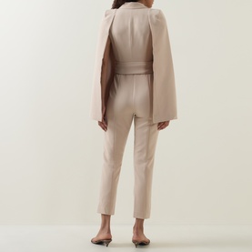 Model wearing Lavish Alice Sand jumpsuit, back view, styled with a matching cape and nude heels.