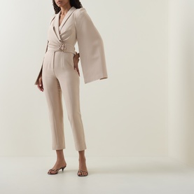 Model wearing Lavish Alice Sand jumpsuit with wide cape sleeves, wrap front, and tapered trousers, styled with strappy heeled sandals