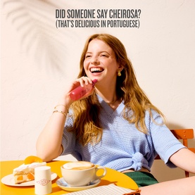 Model with Sol De Janeiro Leite Nectar Perfume Mist, laughing at caf&eacute; table with coffee and pastries