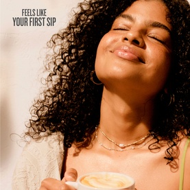 Model with Sol De Janeiro Leite Caf&eacute; Perfume Mist, eyes closed, holding a warm drink, wearing gold hoop earrings and layered necklaces