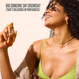 Model with Sol De Janeiro Leite Caf&eacute; Perfume Mist, spraying fragrance, wearing gold chain necklace and earrings with green top