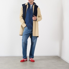 Model wearing A.P.C. washed indigo cotton casual shirt, styled with beige coat, navy gilet, blue jeans and red loafers.