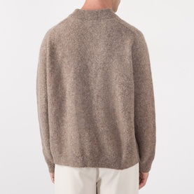 Model wearing A.P.C. taupe crew neck knit sweater, back view, styled with white trousers. Wool-alpaca blend with ribbed collar and cuffs.