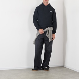 Model wearing A.P.C. black cotton hoodie with small chest logo, styled with grey shirt tied at waist and dark trousers.