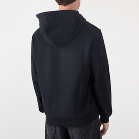 Model wearing A.P.C. black cotton hoodie, rear view showing hood and ribbed cuffs, styled with dark striped trousers.