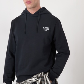 Model wearing A.P.C. black cotton hoodie with small chest logo print, styled with striped trousers.