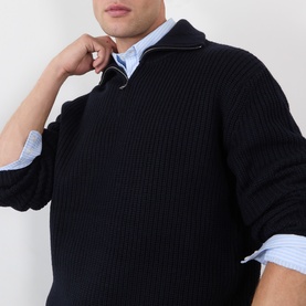 Model wearing A.P.C. dark navy ribbed wool half-zip jumper over a light blue striped shirt, hand raised to collar.