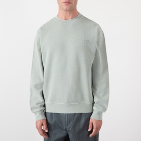 Model wearing A.P.C. Fernando Logo Sweatshirt in gray green, crew neck with chest logo print, styled with striped trousers.