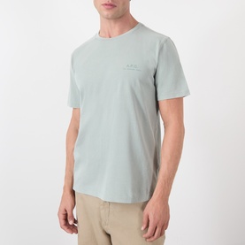 Model wearing A.P.C. gray green cotton T-shirt with small chest logo, styled with beige trousers