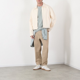 Model wearing A.P.C. gray green cotton T-shirt, styled with cream zip jacket, beige trousers and white trainers