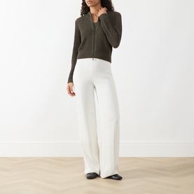 Model wearing Akris Punto olive cotton zip-up cardigan, styled with wide-leg white trousers and black flat shoes.