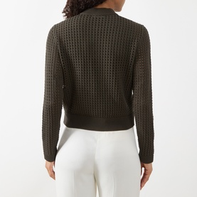 Model wearing Akris Punto olive cotton cardigan, back view, showing textured open-knit pattern and ribbed hem, styled with white trousers