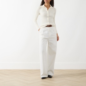 Model wearing Akris Punto cream wool cardigan with collar and button front, styled with wide-leg white trousers and brown belt