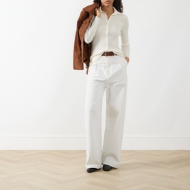 Model wearing Akris Punto cream wool cardigan with white wide-leg trousers, brown belt and black shoes, styled with a tan jacket