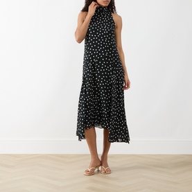 Model wearing Akris Punto black-cream polka dot sleeveless midi dress with high neck and tiered asymmetric hem, styled with gold sandals