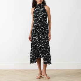 Model wearing Akris Punto black-cream polka dot sleeveless midi dress with high neck and asymmetric hem, styled with nude flat sandals.