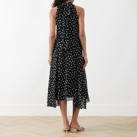 Model wearing Akris Punto black-cream polka dot sleeveless midi dress with halterneck and tiered skirt, styled with gold sandals.