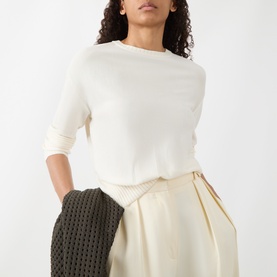 Model wearing Akris Punto cream virgin wool knit top with elbow-length sleeves, styled with cream wide-leg trousers and dark knit jacket.