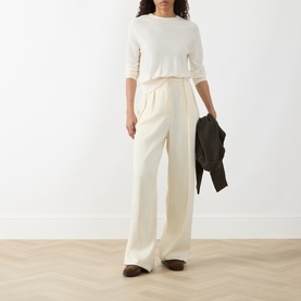 Model wearing Akris Punto cream 100% virgin wool knit top with wide-leg cream trousers, carrying a dark jacket.