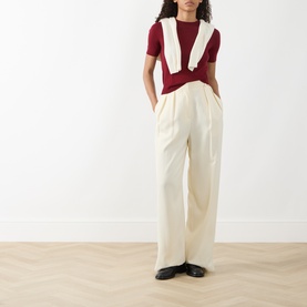 Model wearing Akris Punto Pomegranate wool knit top, styled with cream wide-leg trousers and a white vest draped over shoulders.