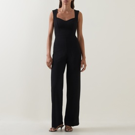 Model wearing Club London black sleeveless wide-leg jumpsuit with sweetheart neckline, styled with gold strappy sandals.