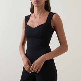 Model wearing Club London black sleeveless dress with sweetheart neckline and fitted bodice, styled with matching black trousers.