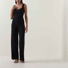 Model wearing Club London black wide-leg jumpsuit with sweetheart neckline and square straps, styled with tan heeled sandals