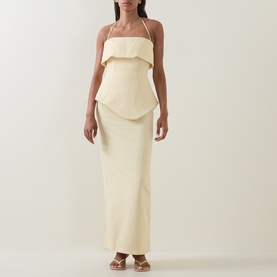 Model wearing cream halterneck maxi dress with layered ruffle bodice and column skirt, styled with strappy sandals