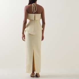 Model wearing a cream halterneck maxi dress with peplum detail, tie-back neckline and back split, shown from behind.