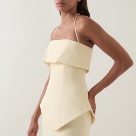 Model wearing a pale yellow structured strapless mini dress with folded panel detail and thin halterneck straps, cropped view