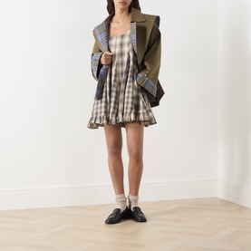 Model wearing Damson Madder Cardamon Mix Check cotton mini dress with ruffle hem, styled with olive blazer and black loafers