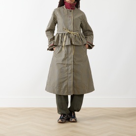Model wearing Damson Madder Navy Gingham coat with ruffle hem and cuffs, belted waist, styled with green trousers and brown shoes.