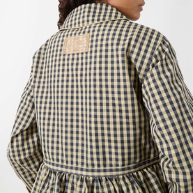 Model wearing Damson Madder navy gingham outerwear, back view showing branded patch, gathered waist, and long sleeves.