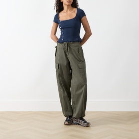 Model wearing Damson Madder navy short-sleeve square-neck ribbed top with button front, styled with khaki cargo trousers and chunky trainers.