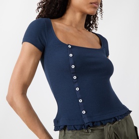 Model wearing Damson Madder navy ribbed short-sleeve top with square neckline, button front, and frill hem. Styled with khaki trousers.
