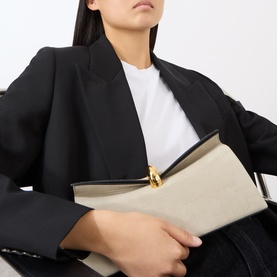 Model carrying a cream clutch bag with gold hardware, styled with a black blazer and white tee