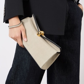 Model carrying a cream leather clutch bag with gold ring hardware, styled with a black blazer and dark jeans