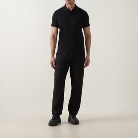 Model wearing Moose Knuckles black cotton polo shirt with short sleeves, paired with black cargo trousers and dark trainers.
